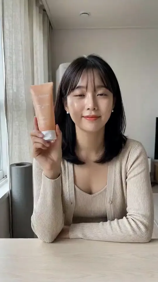 Clip from the One product, three AI influencers template: Vertical lifestyle video in her bright apartment: she holds the sunscreen tube up toward the lens, turns the label to face it and says, softly and clearly: "Last step of the morning: Solenne SPF fifty. Two finger-lengths, every day." Then she smiles and sets it down. Handheld phone camera, soft morning light. No music, no subtitles, no on-screen text.